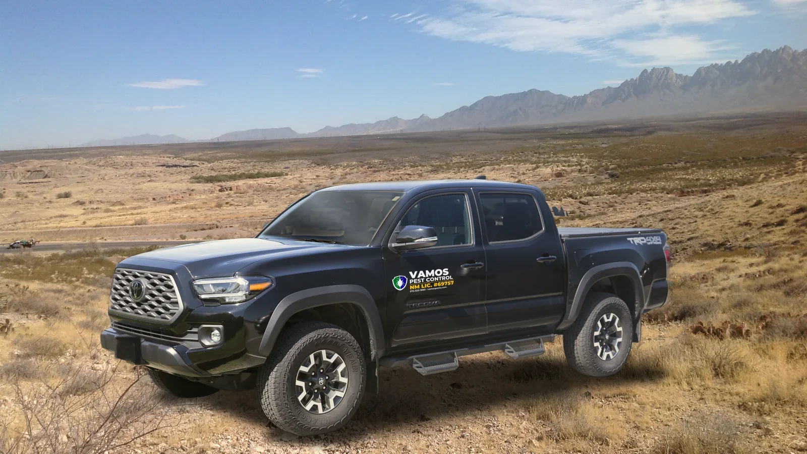 Black 2022 Toyota Tacoma with the Vamos Pest Control door decal (NM license 69757, phone 575-323-1880), parked in the desert outside Las Cruces with the Organ Mountains behind it